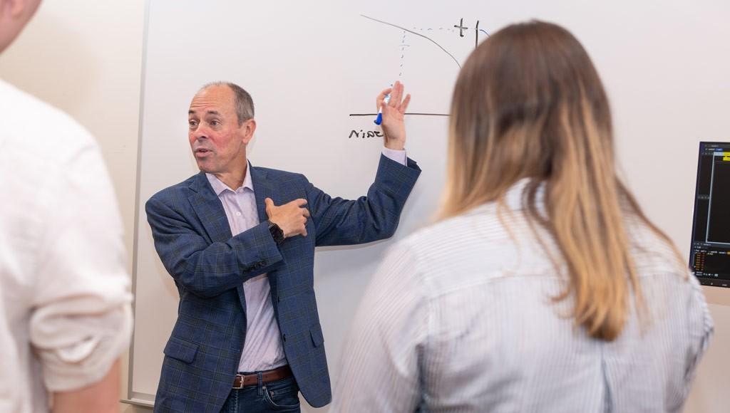 A professor explains a graph on a whiteboard